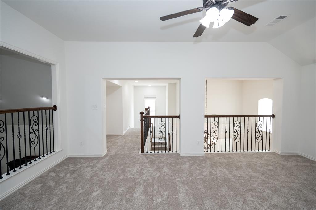 Vaulted ceiling with a ceiling fan, carpeted flooring, and decorative wrought iron railings
