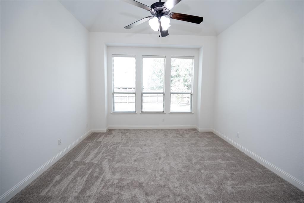 Recessed window bay, gray carpet, multiple windows with blinds, ceiling fan with light fixture, and white wall finishes