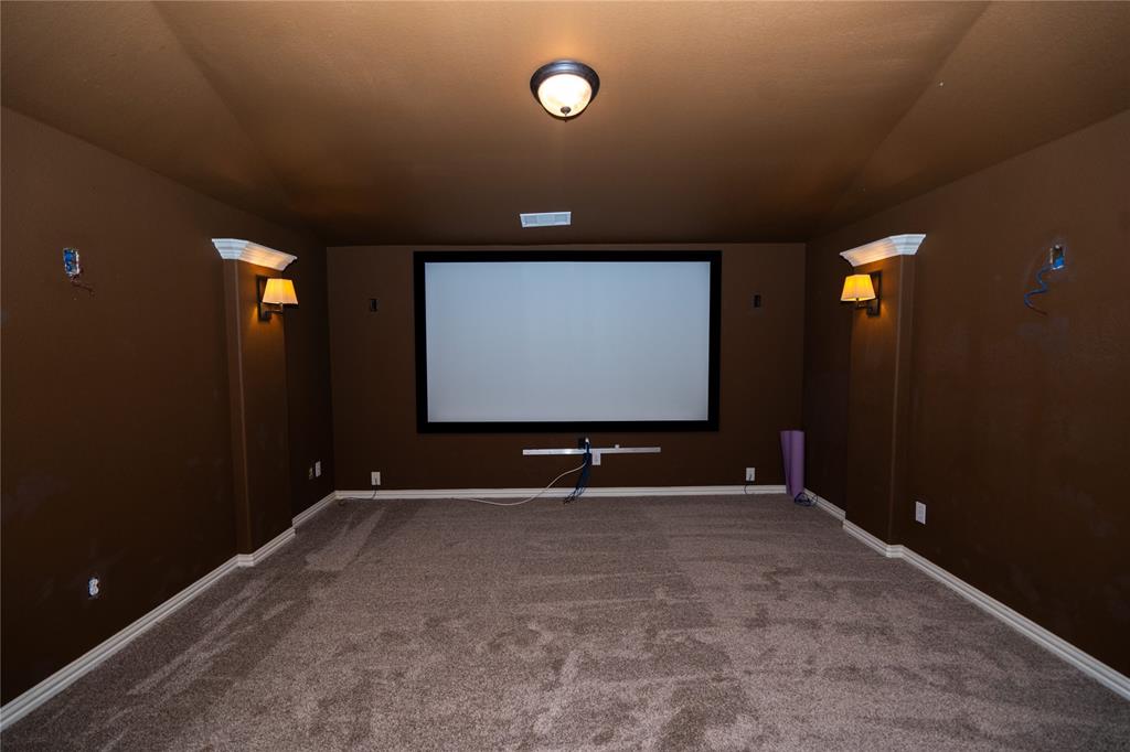 Dedicated media room featuring a large projection screen, built-in wall sconces, and recessed overhead lighting