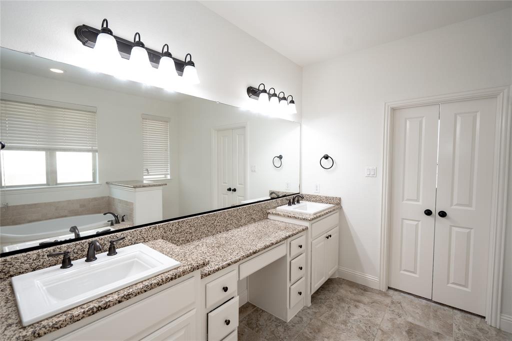 Dual vanity with granite countertops, integrated sinks, white cabinetry, and matte black hardware