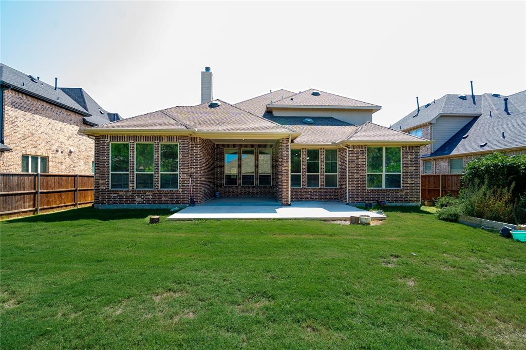 Expansive rear lawn featuring a large concrete patio, brick exterior, and multiple windows