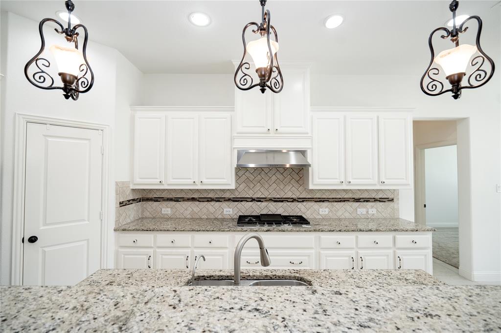 Kitchen featuring an island with a stainless steel sink and faucet, white cabinetry, granite countertops, and a herringbone tile backsplash