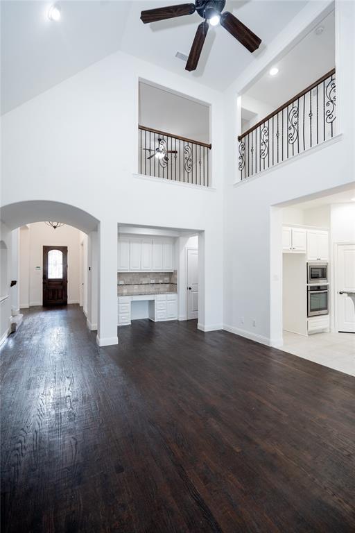 Soaring vaulted ceilings with a ceiling fan, dark wood-finish flooring, white built-in cabinetry with a desk area, and a wrought iron banister