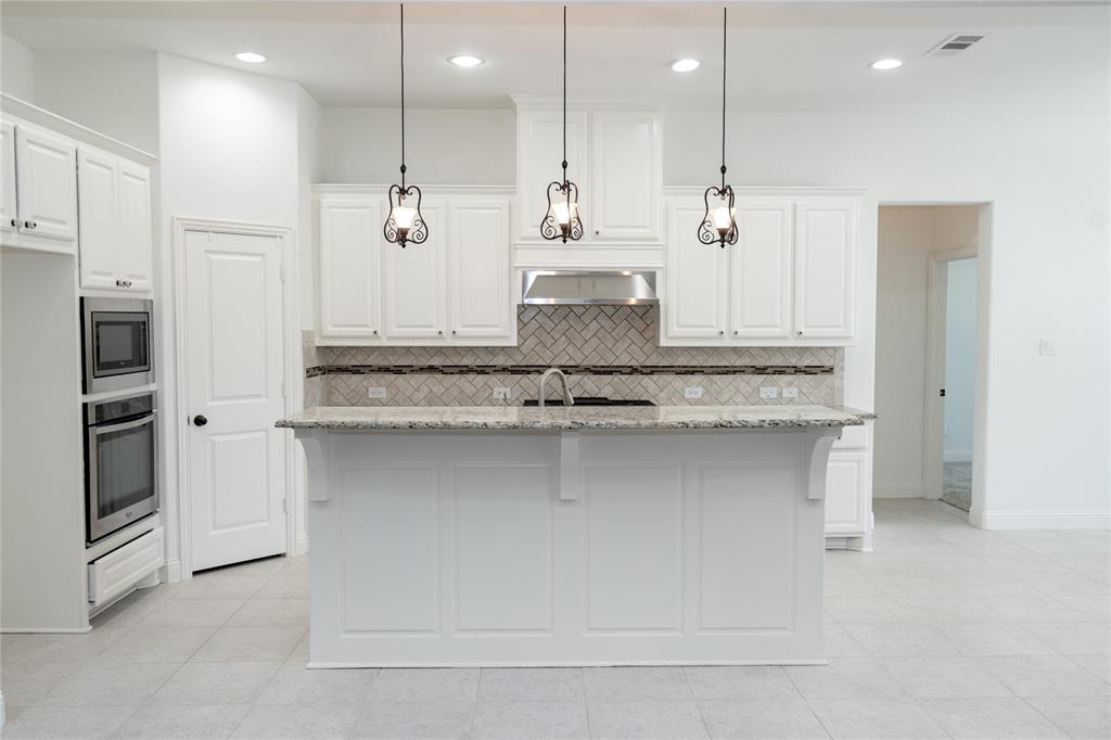 Kitchen featuring a central island with an integrated sink, white cabinetry, a herringbone tile backsplash, stainless steel appliances, and pendant lighting