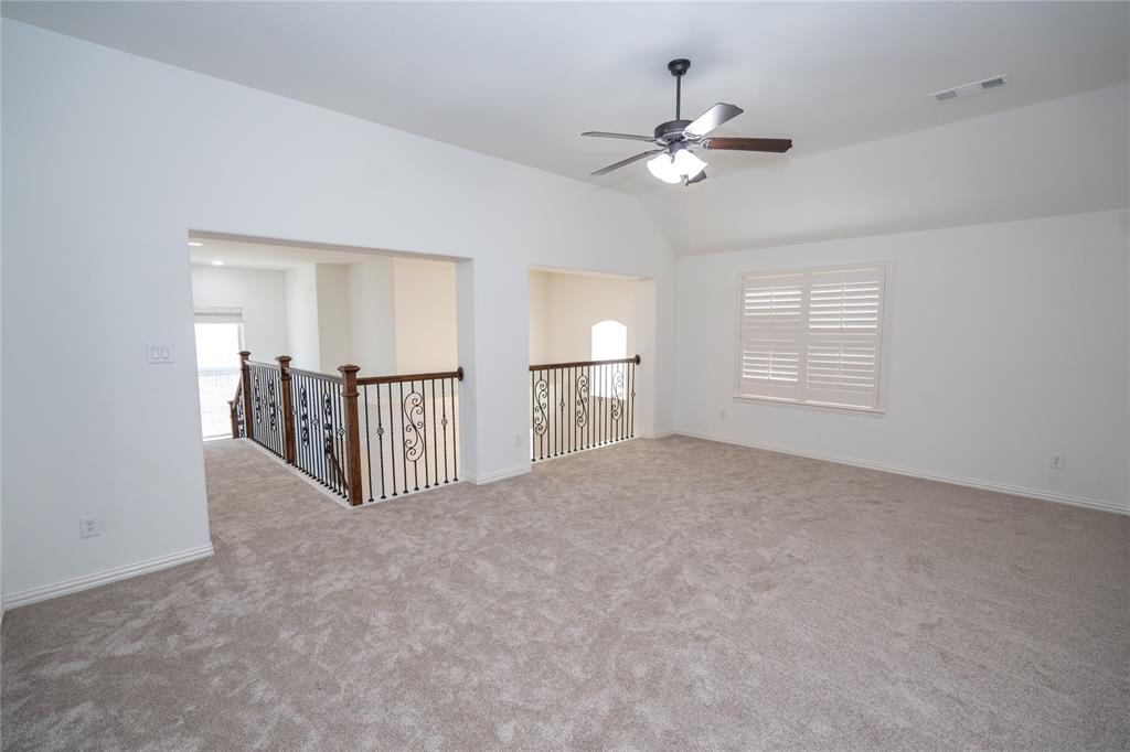 Carpeted loft space featuring a vaulted ceiling, ceiling fan with light, window with plantation shutters, and ornate metal railings