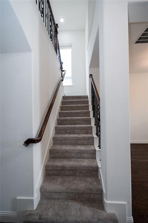 Carpeted staircase featuring wrought iron balusters and a dark wood handrail