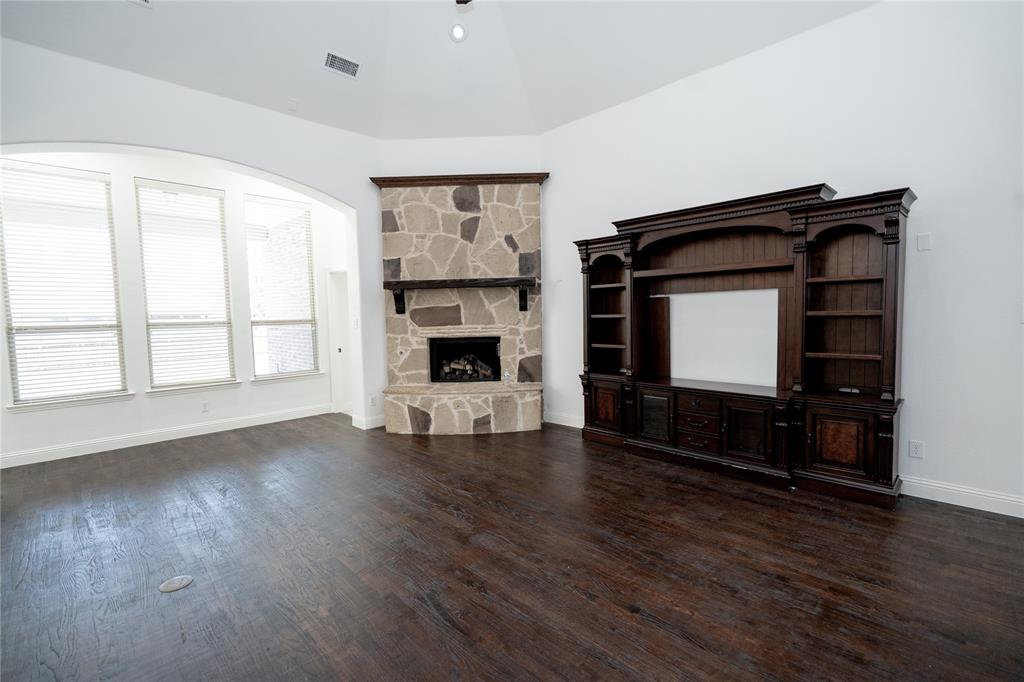 Vaulted ceiling, stone-clad fireplace with mantel, dark wood-finish flooring, built-in entertainment center, and multiple windows with blinds