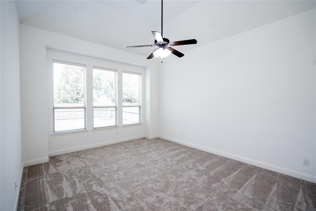 Vaulted ceiling, three large windows with blinds, ceiling fan with light fixture, neutral-toned carpet, and white walls