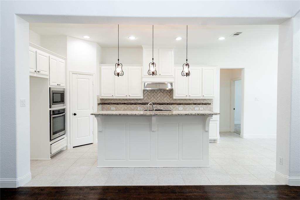 White cabinetry with stainless steel appliances, a kitchen island with pendant lighting, a tile backsplash, and light-toned tile flooring