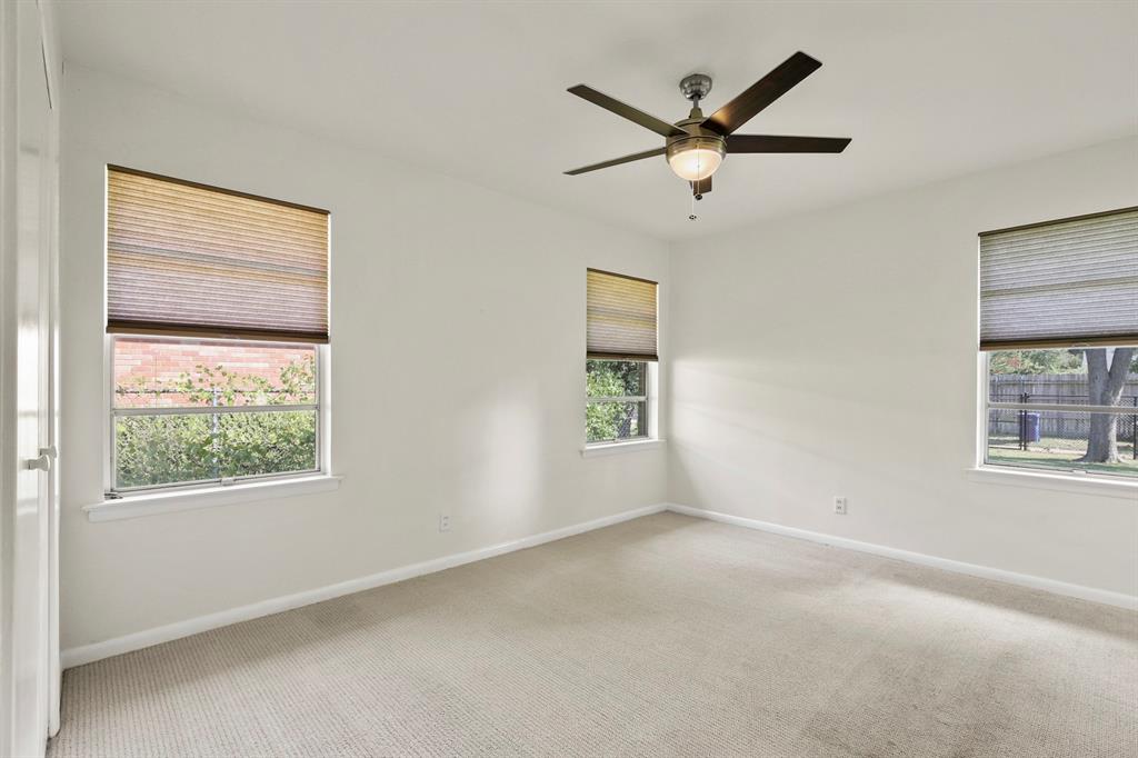 Neutral wall paint, three windows with cellular shades, ceiling fan with integrated lighting, and carpeted flooring