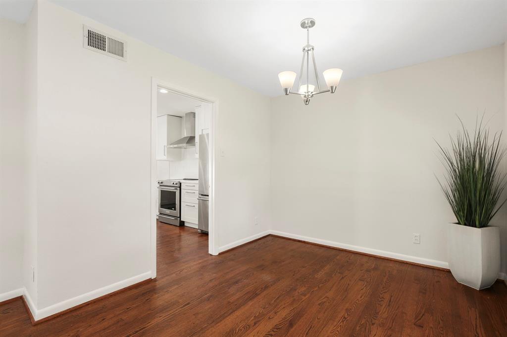 Hardwood flooring, contemporary chandelier, crisp white walls, and a recessed kitchen entry
