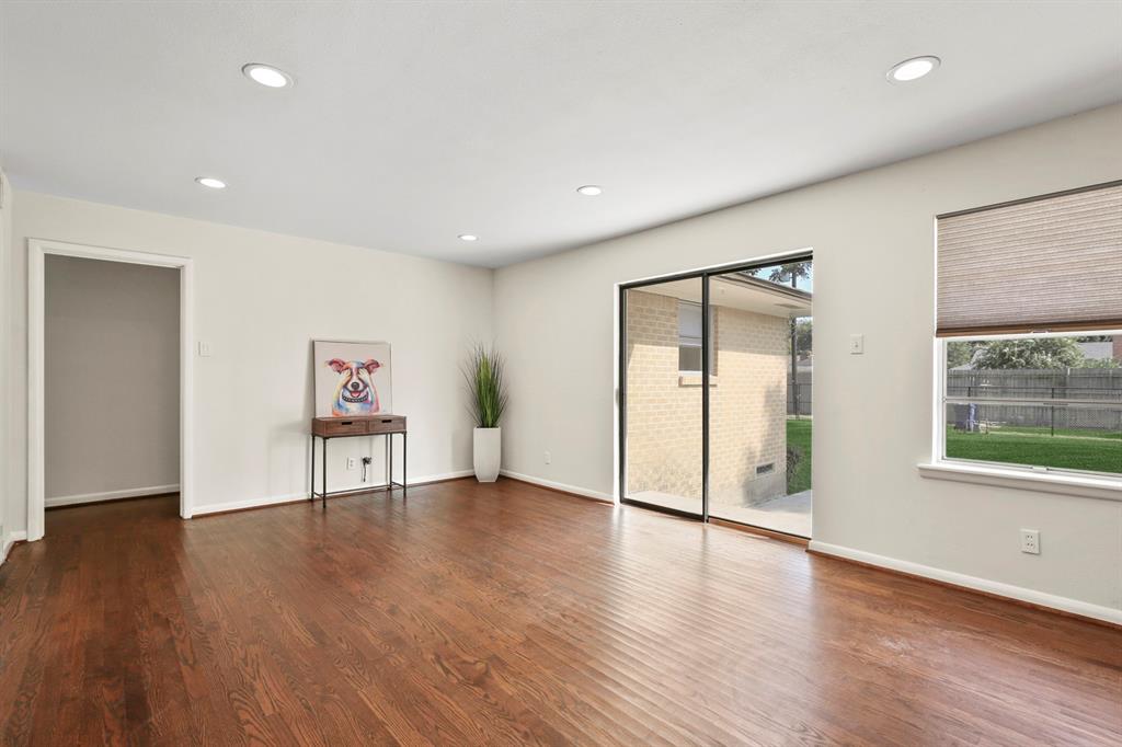 Recessed lighting illuminates the wood-finish flooring, complemented by a sliding glass door and a large window with privacy blinds