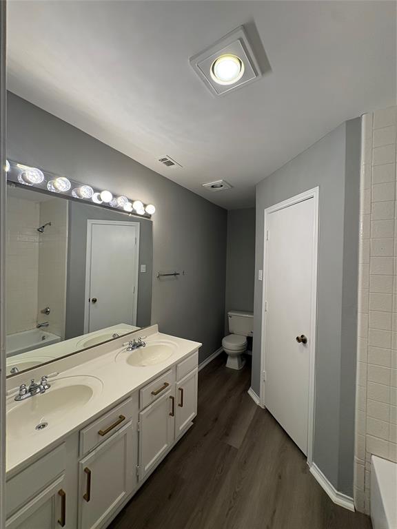 Dual vanity with integrated sinks, wood-finish flooring, and white cabinetry with brass-toned hardware Dual vanity with integrated sinks, wood-finish flooring, and white cabinetry with brass-toned hardware