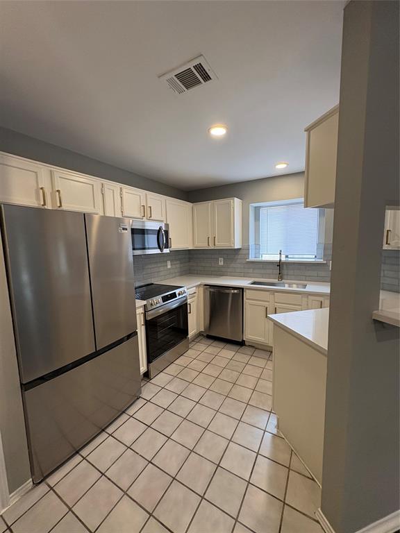 Stainless steel appliances, white cabinetry, tile flooring, light-toned countertops, and a subway tile backsplash Stainless steel appliances, white cabinetry, tile flooring, light-toned countertops, and a subway tile backsplash