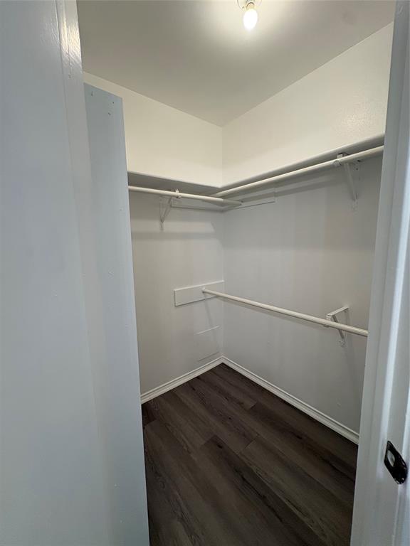 Walk-in closet featuring wood-finish flooring, white walls, and built-in shelving with hanging rods Walk-in closet featuring wood-finish flooring, white walls, and built-in shelving with hanging rods