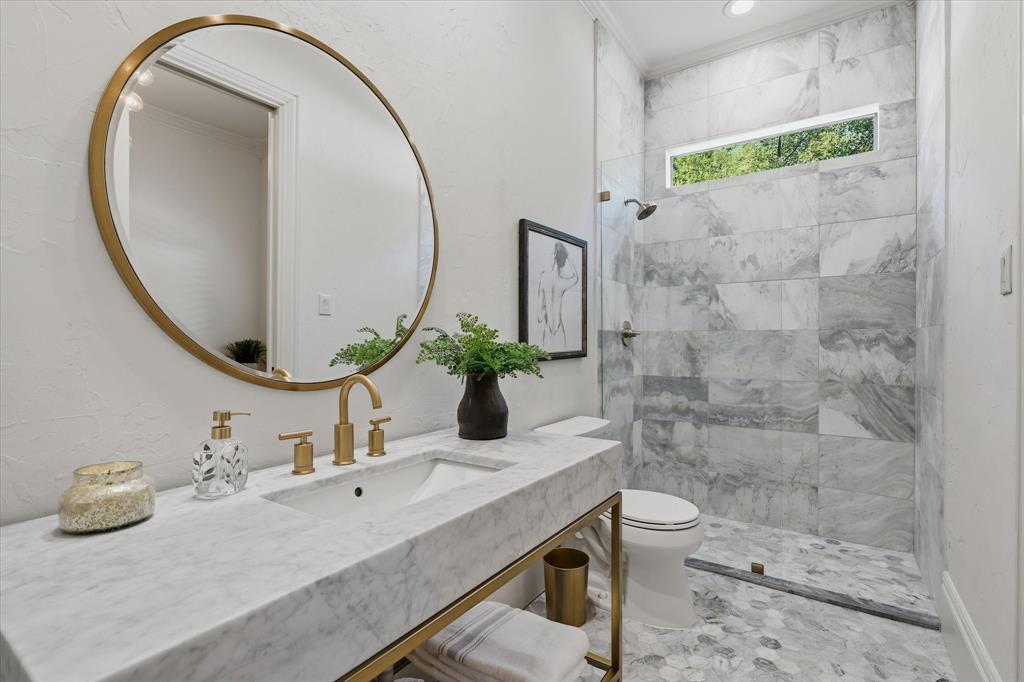 First floor guest ensuite bath is beautifully remodeled featuring marble finishes, a glass-enclosed shower and refined brass fixtures.
