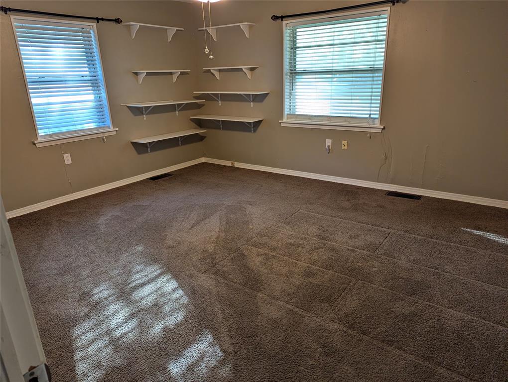 Bedroom #3 – View 1: Spacious secondary bedroom located in the southeast corner of the home, featuring two windows overlooking the front yard, carpeted flooring, and built-in corner shelving.