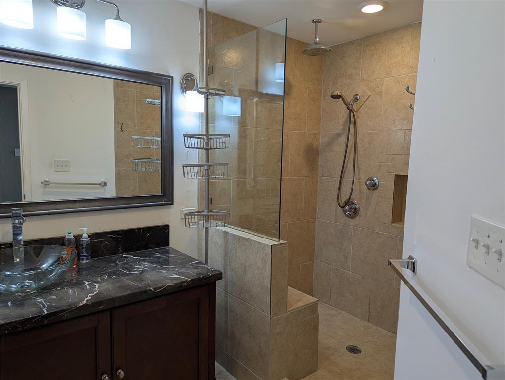 View 1: Updated ensuite bathroom featuring a dark vanity, granite-look countertop, framed mirror, and spacious tiled walk-in shower.