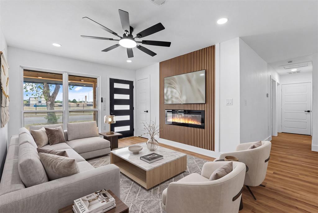 Recessed lighting, wood-finish flooring, a modern ceiling fan, an accent wall with an electric fireplace, and large windows Recessed lighting, wood-finish flooring, a modern ceiling fan, an accent wall with an electric fireplace, and large windows