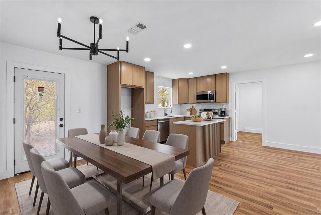 Open-concept living area featuring wood-finish flooring, a modern chandelier, light wood cabinetry, white countertops, and a full-light exterior door