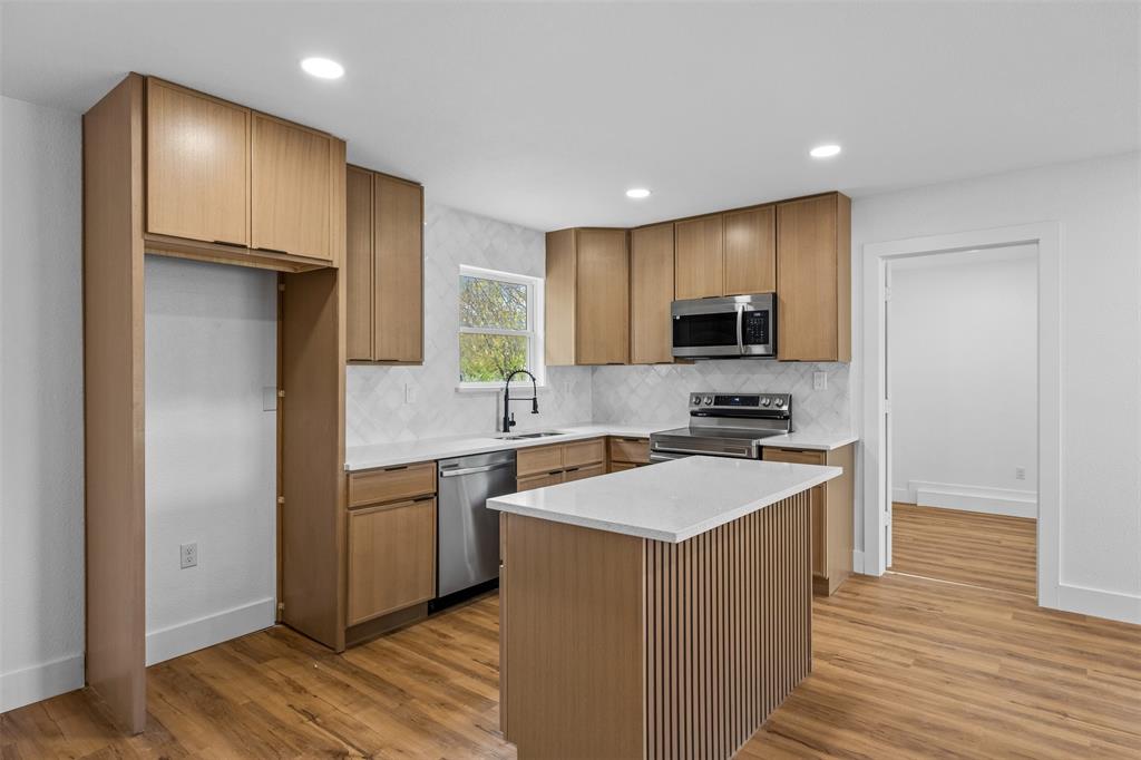 Modern kitchen featuring wood-finish cabinetry, stainless steel appliances, a white quartz countertop island, and wood-finish flooring