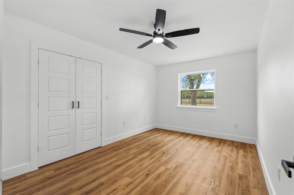 Wood-finish flooring, white paneled double doors, black ceiling fan with integrated lighting, and a white-framed window