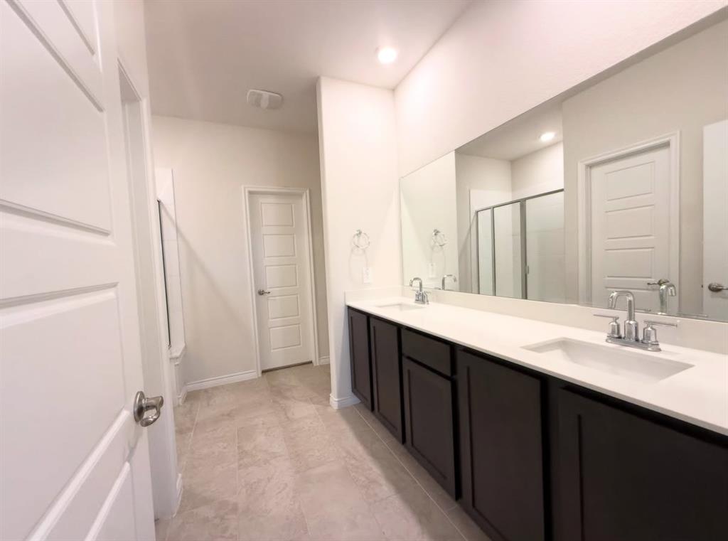 Dual-sink vanity with dark cabinetry, solid-surface countertop, full-width vanity mirror, and tile flooring