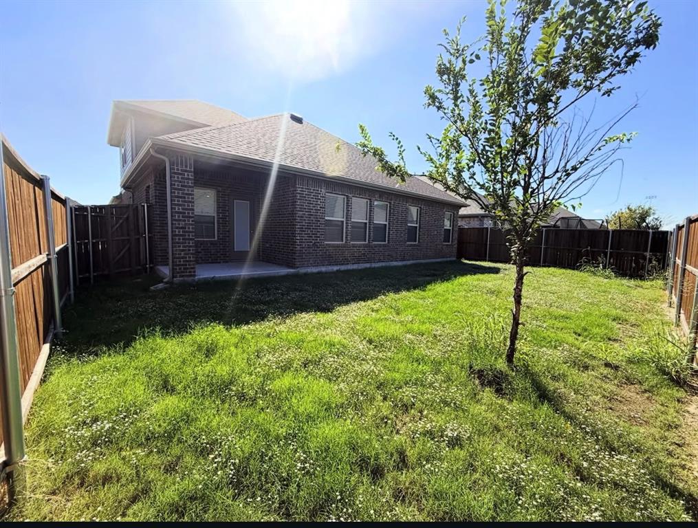 Brick exterior featuring a concrete patio, wood privacy fencing, and a sodded yard