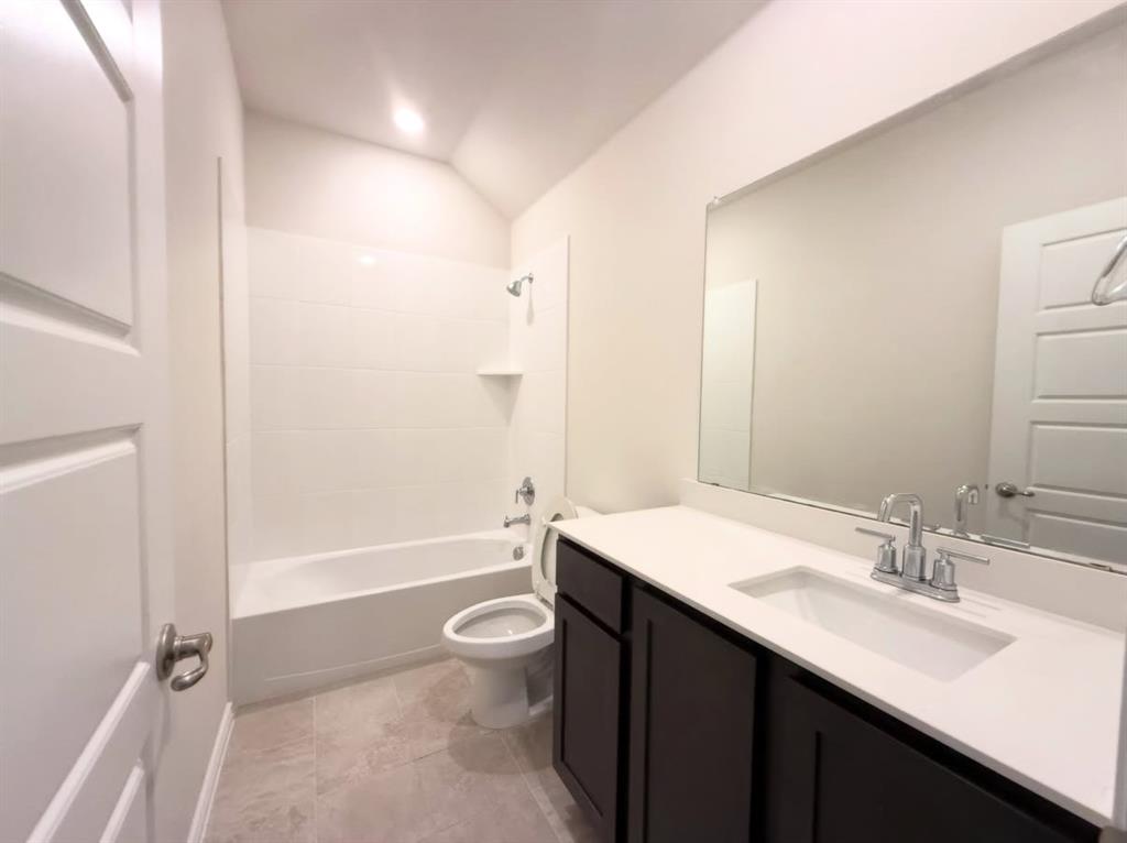 Bathroom featuring a dark-finish vanity with a light-toned countertop, integrated rectangular sink, large wall-mounted mirror, and a tub-shower combination with light-toned wall tile