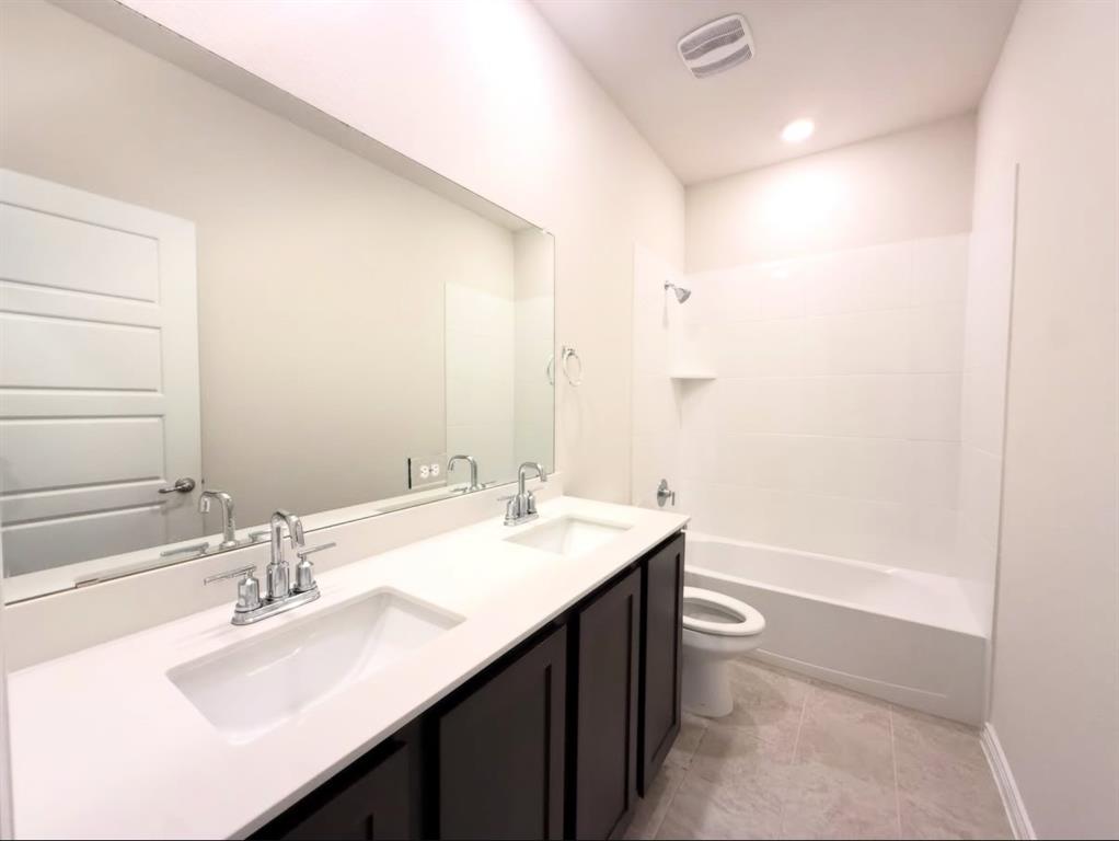 Dual-sink vanity with white composite countertop, large wall-spanning mirror, dark cabinetry, and tile flooring