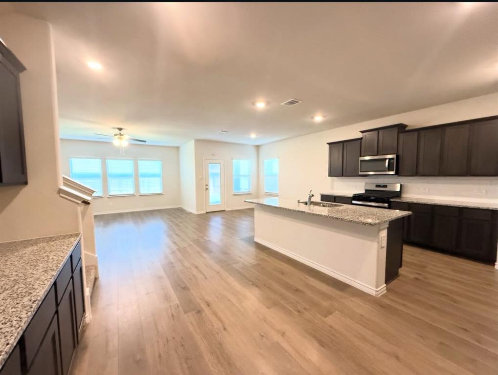 Open-concept space featuring wood-finish flooring, dark-toned cabinetry, stone-finish countertops, stainless steel appliances, and recessed lighting