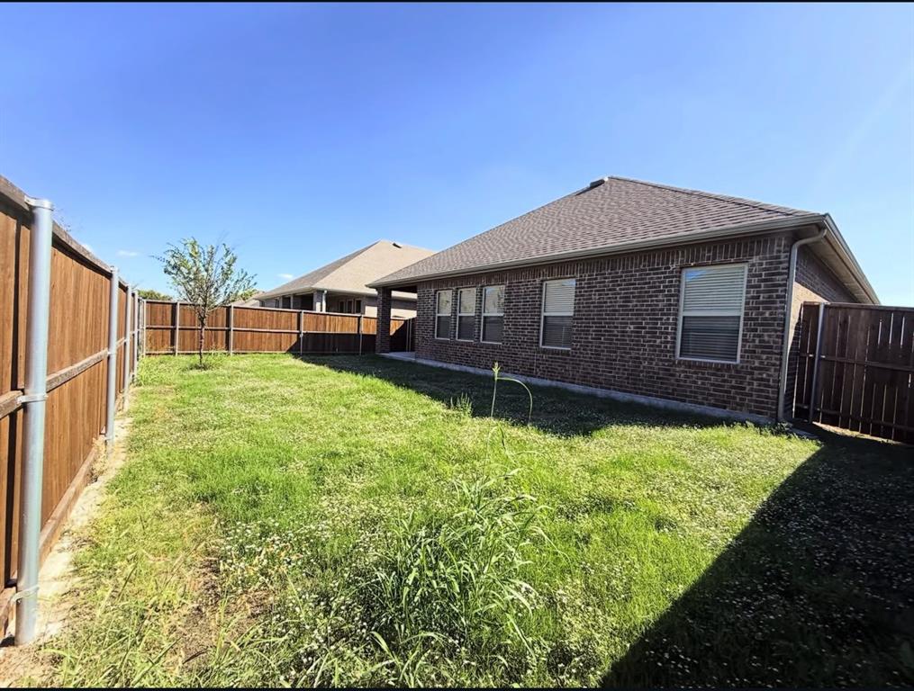 Backyard featuring a brick exterior, shingle roofing, and a wooden perimeter fence