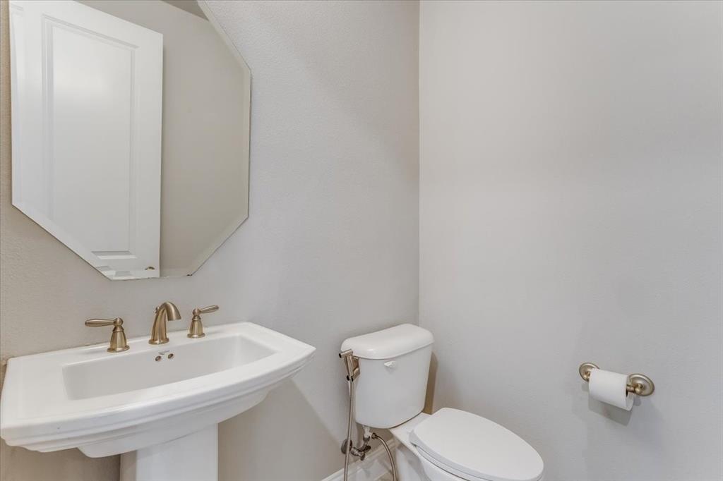 Pedestal sink with brass-finish faucet, octagonal wall mirror, and toilet with brass-finish bidet attachment
