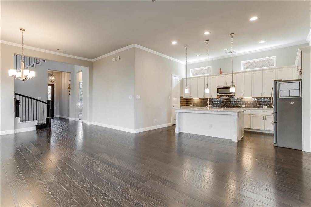 Wood-finish flooring throughout, kitchen with white cabinetry, stainless steel appliances, pendant lighting, and a kitchen island