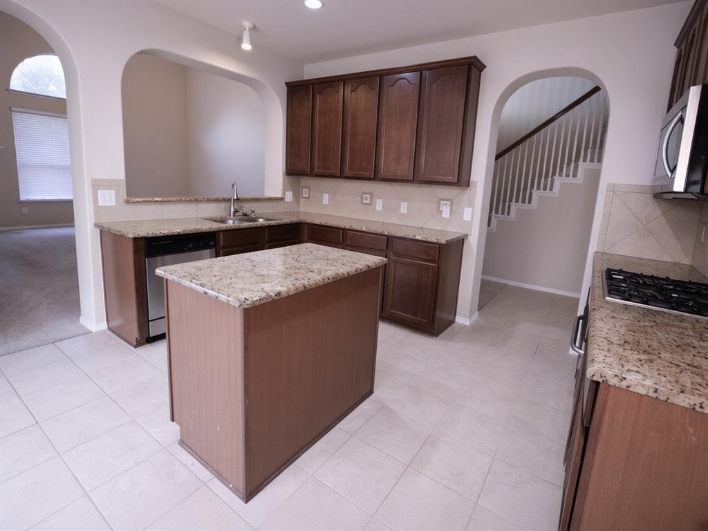 Kitchen featuring a central island, granite countertops, wood cabinetry, stainless steel appliances, and tile flooring