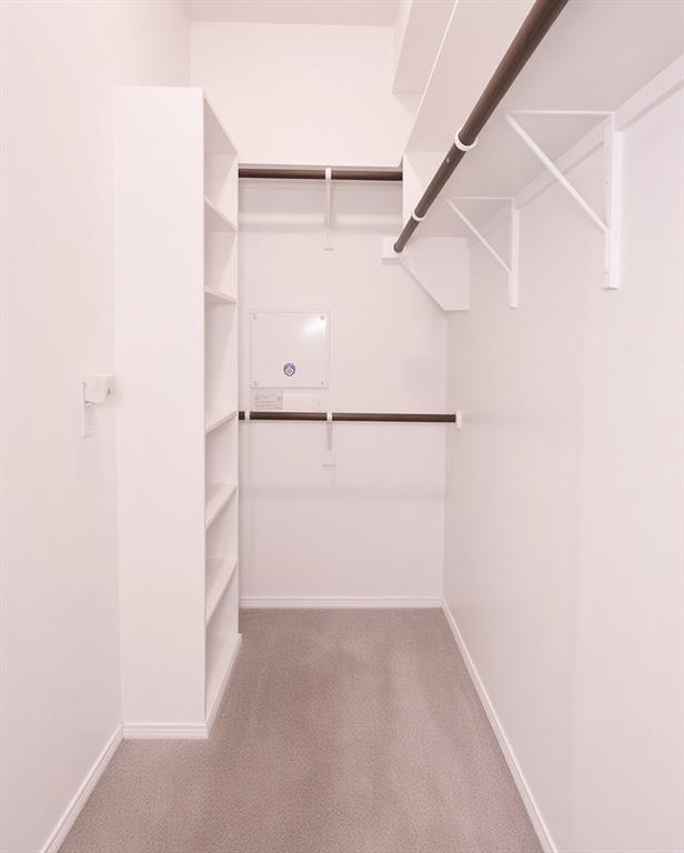 Walk-in closet featuring white built-in shelving, multiple hanging rods, and light gray carpeting