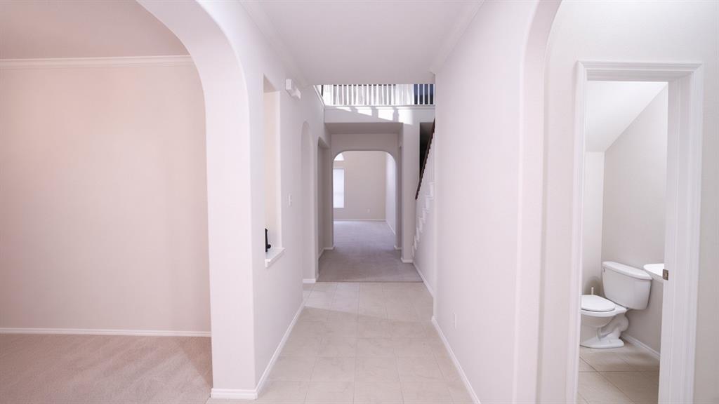 Arched doorways, tile flooring, carpeted room, carpeted stairway with white balusters, and a powder room with a commode and pedestal sink