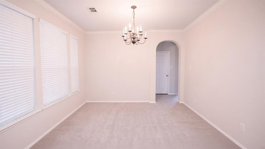 Room featuring light-toned carpeting, multiple windows with blinds, crown molding, and a chandelier