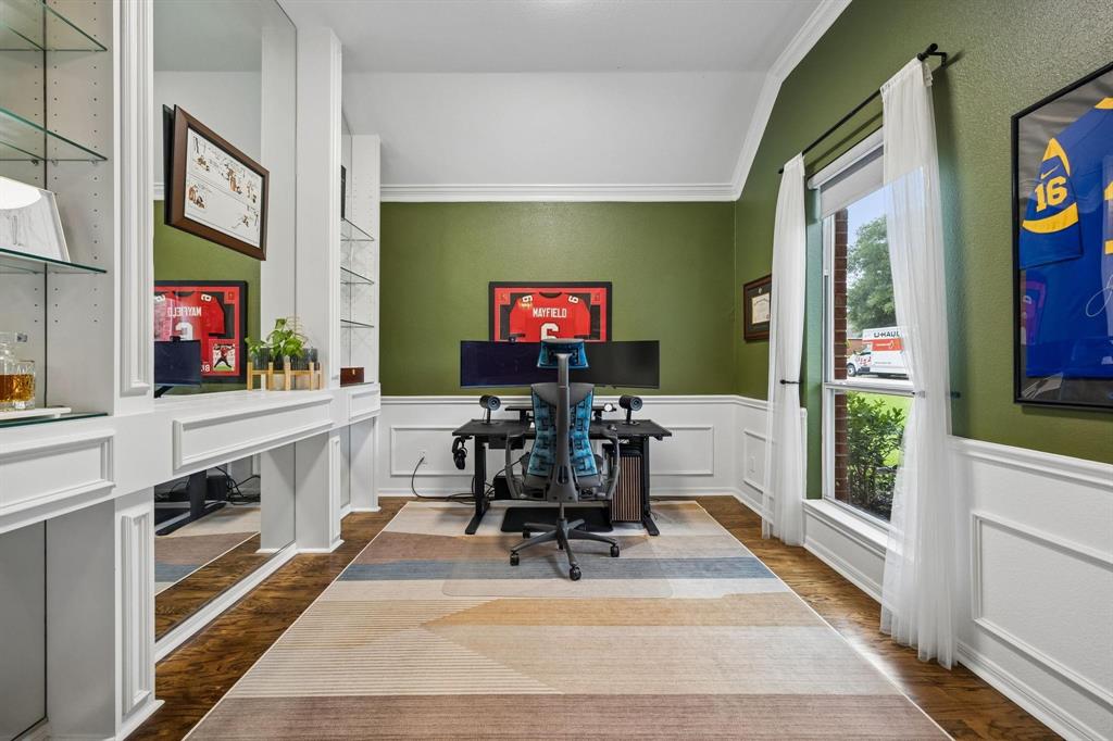 Built-in shelving with glass inserts, dedicated desk area, wood-finish flooring, accent wall, and crown molding