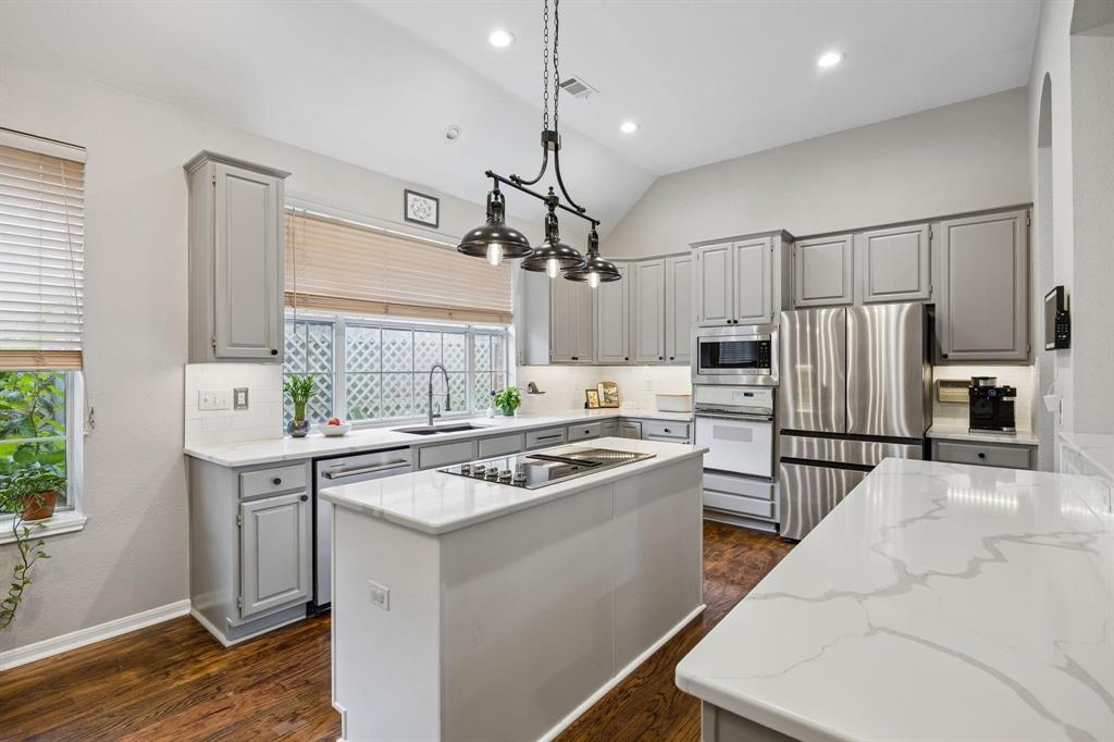 Kitchen featuring gray cabinetry, white countertops, stainless steel appliances, a central island with cooktop, and wood-finish flooring