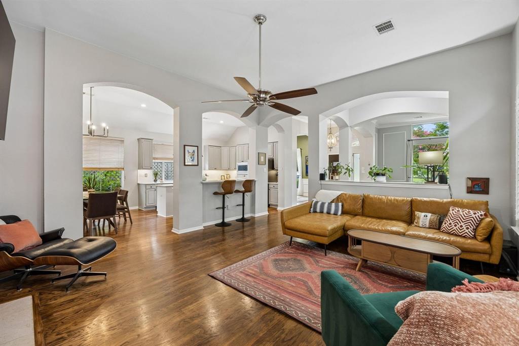 Hardwood flooring with a polished finish, arched doorways, vaulted ceiling, and a ceiling fan with light fixture