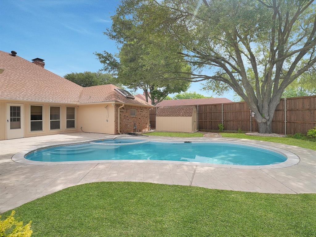 In-ground swimming pool with integrated spa, concrete decking, mature tree, manicured lawn, and privacy fence