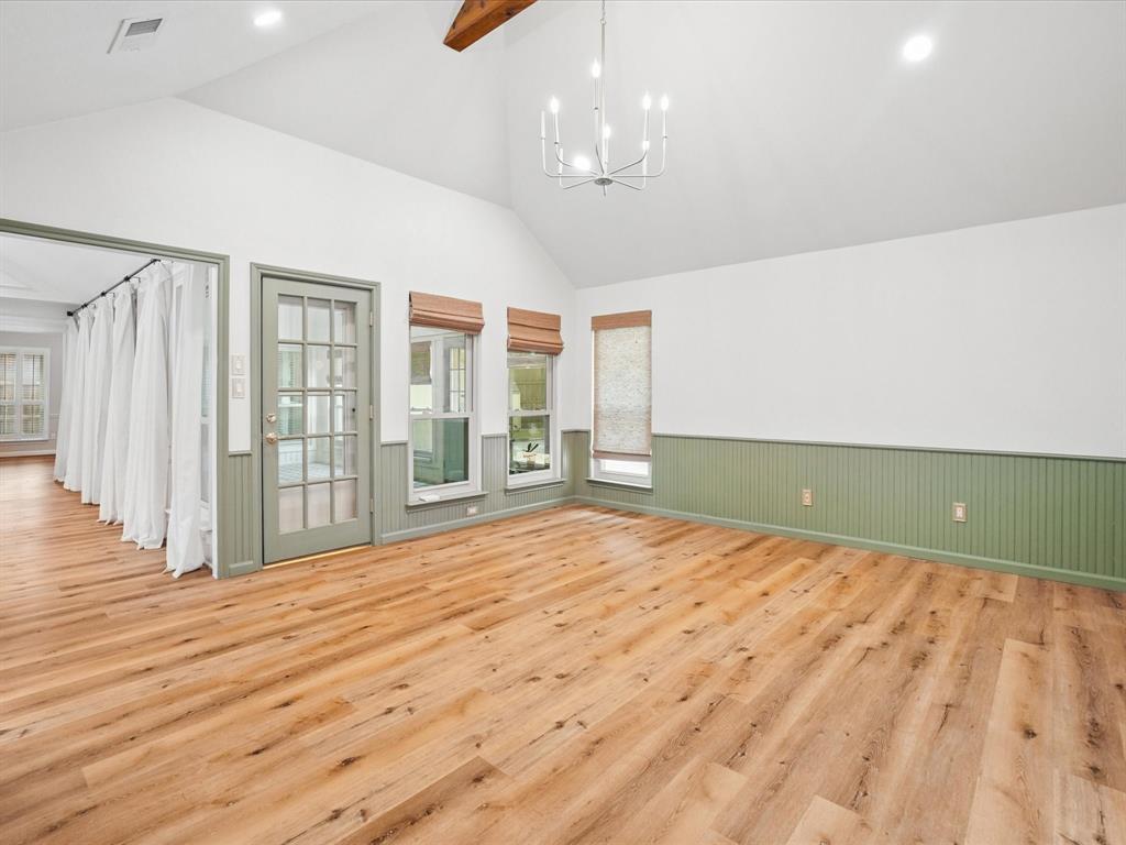 Vaulted ceiling with an exposed wood beam, wood-finish flooring, two large windows, a glass-paned door, and beadboard wainscoting