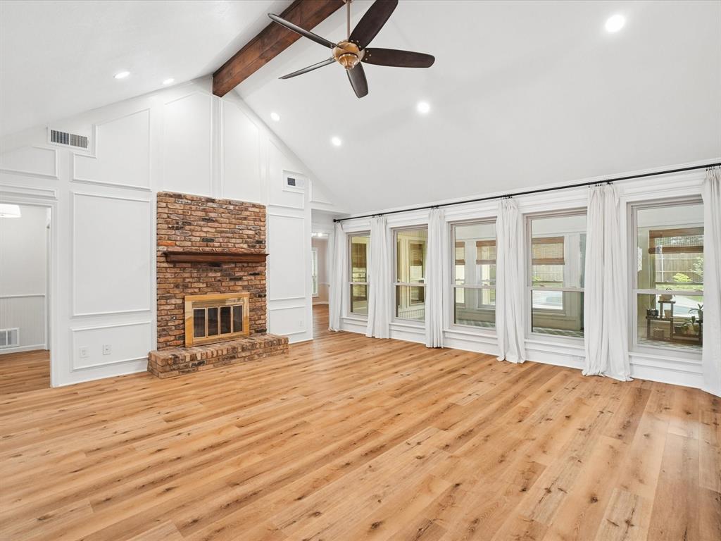 Vaulted ceilings with exposed wood beam, recessed lighting, wood-finish flooring, brick fireplace with wood mantel, and a wall of windows