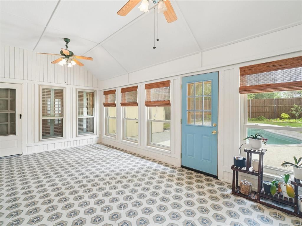 Vaulted ceiling with exposed beams, decorative ceiling fans, patterned tile flooring, multiple windows with blinds, and an exterior door with glass panels