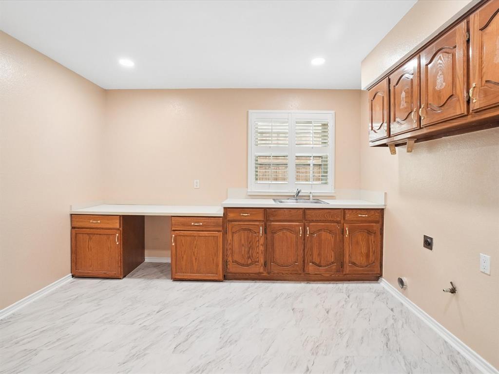 Functional utility room featuring wood-finish cabinetry, white countertops, and a stainless steel sink
