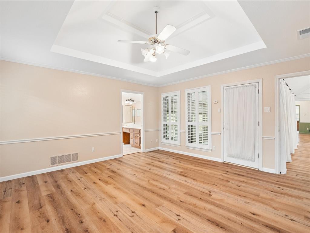 Tray ceiling with a ceiling fan, wood-finish flooring, white window shutters, and chair rail molding