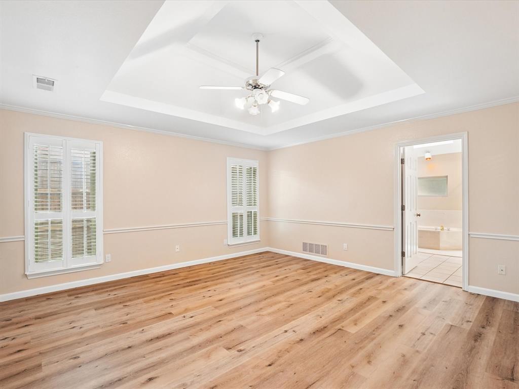 Tray ceiling with a ceiling fan, wood-finish flooring, two windows with plantation shutters, and crown molding