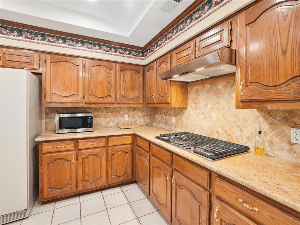Recessed ceiling with an overhead light fixture, wood-finish cabinetry, tile flooring, and a built-in gas cooktop