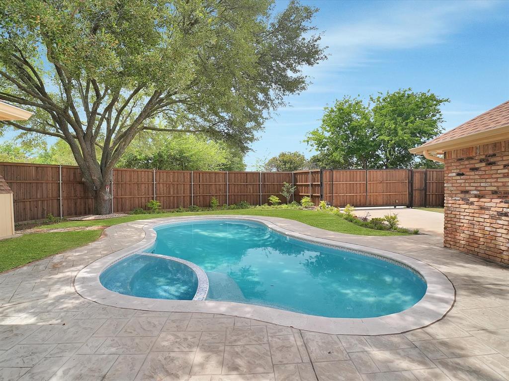Private backyard featuring a free-form swimming pool with integrated spa, stamped concrete decking, mature shade trees, and a wood privacy fence